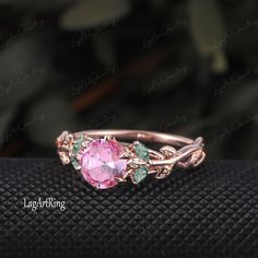 a pink ring with green leaves on the side and an oval stone in the middle