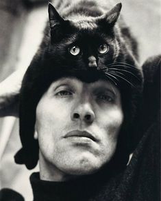 a black cat is sitting on top of a man's head while he looks at the camera