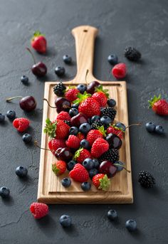 fresh berries and cherries are arranged on a cutting board with a wooden spatula