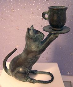 a cat holding a cup and saucer on top of a white table next to a purple wall