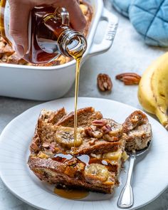 someone pouring maple syrup on top of french toast with bananas and pecans in the background