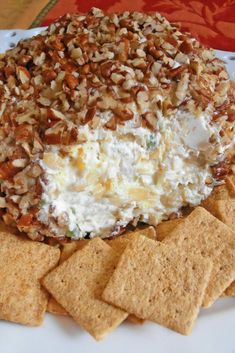 a white plate topped with crackers and cheese covered in nuts next to crackers