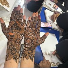 two hands with henna designs on them and some people sitting at a table in the background