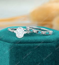 two wedding rings sitting on top of a green velvet ring box with blue and white stones