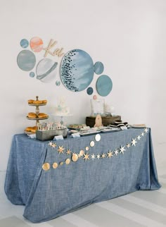 a blue table topped with lots of desserts next to a wall mounted art piece