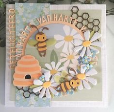 a close up of a greeting card with flowers and bees on the front, and a beehive in the back