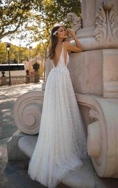 a woman in a white dress leaning against a stone pillar with her back to the camera