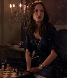 a woman sitting at a chess board with her hand on the queen's chest