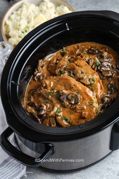 a crock pot filled with chicken and mushrooms covered in gravy next to mashed potatoes