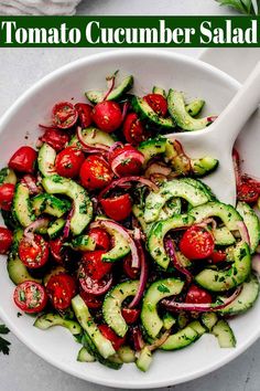 a white bowl filled with cucumber salad and topped with sliced tomatoes, onions, red onion, and green herbs