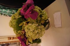 a vase filled with green and pink flowers on top of a white table next to a mirror