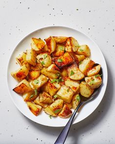 a white plate topped with cooked potatoes on top of a table next to a fork