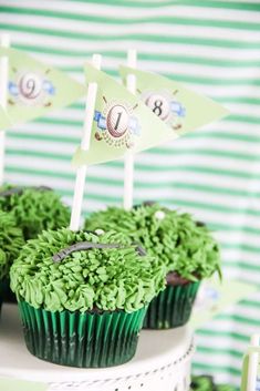 cupcakes with green frosting and small flags on top are sitting on a cake stand