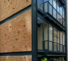 the side of a brick building with windows and balconies on each floor, in front of green plants