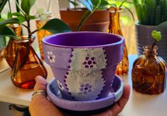 a hand holding a purple flower pot on top of a table next to other vases