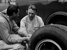 two men sitting next to each other in front of a truck with tires on it