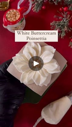 white buttercream poinsettia in a box on a red table with christmas decorations