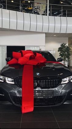 a black car with a red ribbon tied to it's hood in a showroom