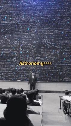 a man standing in front of a blackboard with writing on it and people sitting at desks