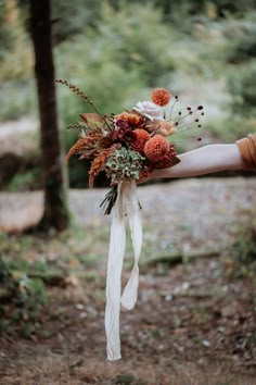 a person holding a bouquet with flowers in their hand on a path through the woods