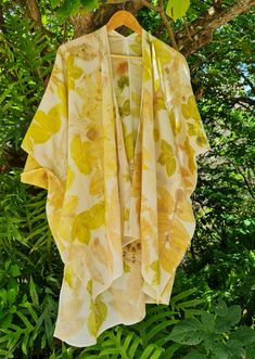 a yellow and white kimono hanging from a tree in front of some green leaves