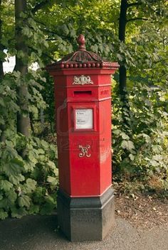 a red post box sitting on the side of a road in front of some trees