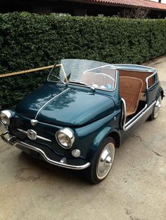 an old fashioned car is parked in front of a hedge on the sidewalk with its door open