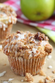 two muffins sitting on top of a table next to green apples