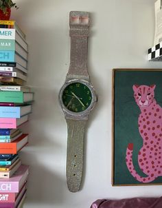 a pink watch sitting on top of a white wall next to books and a painting