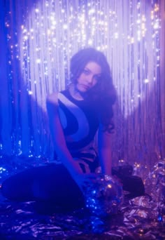 a woman sitting on top of a bed in front of a curtain with lights behind her