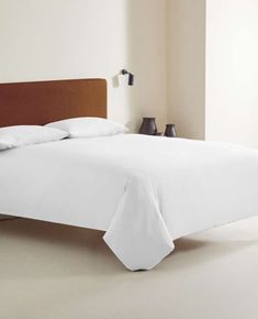 a bed with white sheets and pillows in a clean room, ready to be used as a headboard