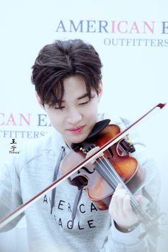 a young man playing the violin in front of an american outfitters sign and wall