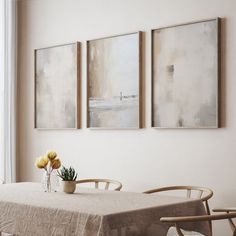 three paintings hang on the wall above a dining room table with two vases filled with yellow flowers