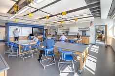 people are sitting at desks in an open room with blue chairs and yellow lights