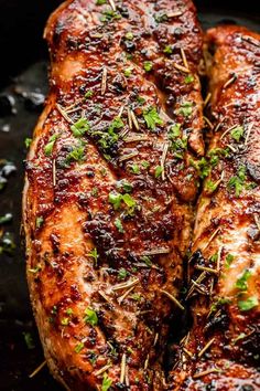 two pieces of meat covered in herbs and seasoning on top of a black surface