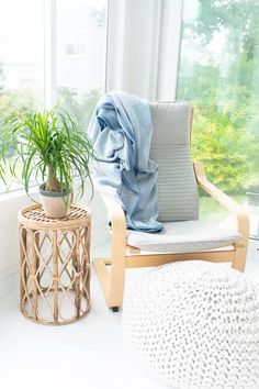 a chair with a blanket on it next to a potted plant in front of a window