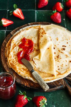 two tortillas on a wooden plate with strawberries next to it and a jar of jam