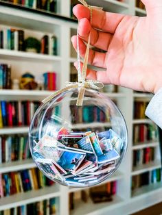 a hand holding a clear glass ball with magazines inside it and bookshelves in the background