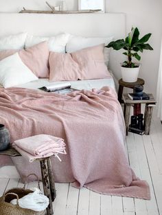 a bed with pink blankets and pillows on top of it next to a wooden stool