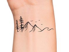 a small wrist tattoo with trees and mountains on the back of its left arm, in black ink