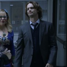 a man and woman standing next to each other in an office building with blinds on the windows