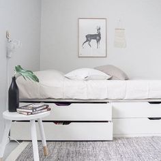 a white bed with two drawers underneath it and a painting on the wall behind it