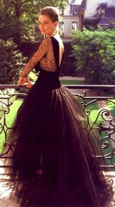 a woman in a black dress standing on a balcony