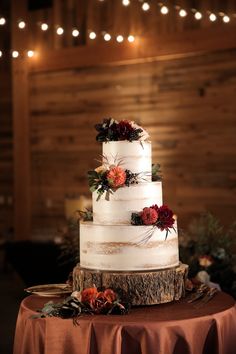 a three tiered cake with flowers and greenery sits on top of a table