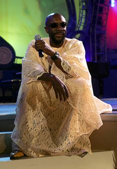 a man sitting on top of a white box holding a microphone in his right hand