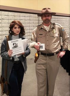 a man and woman dressed in police uniforms standing next to each other holding papers with the same name on them