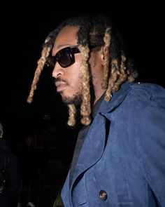 a man with dreadlocks wearing sunglasses and a blue jacket standing in the dark