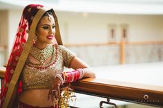 a woman in a red and gold bridal outfit standing next to a wooden railing