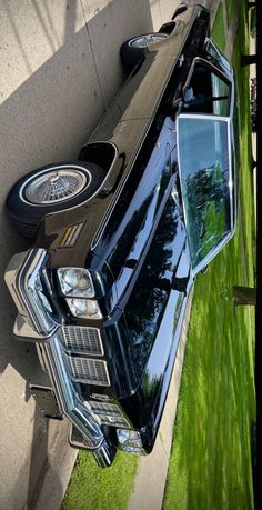 a black car parked on the side of a road next to a grass covered sidewalk