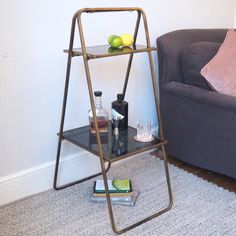 a glass shelf with bottles and glasses on it in front of a gray couch next to a blue sofa